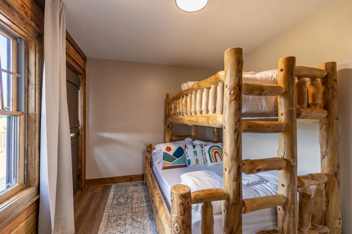 A playful bunk room featuring a sturdy wooden bunk bed with colorful decorative pillows and a cozy rug. The space is bright, inviting, and designed with children or families in mind, promoting both fun and restful sleep.