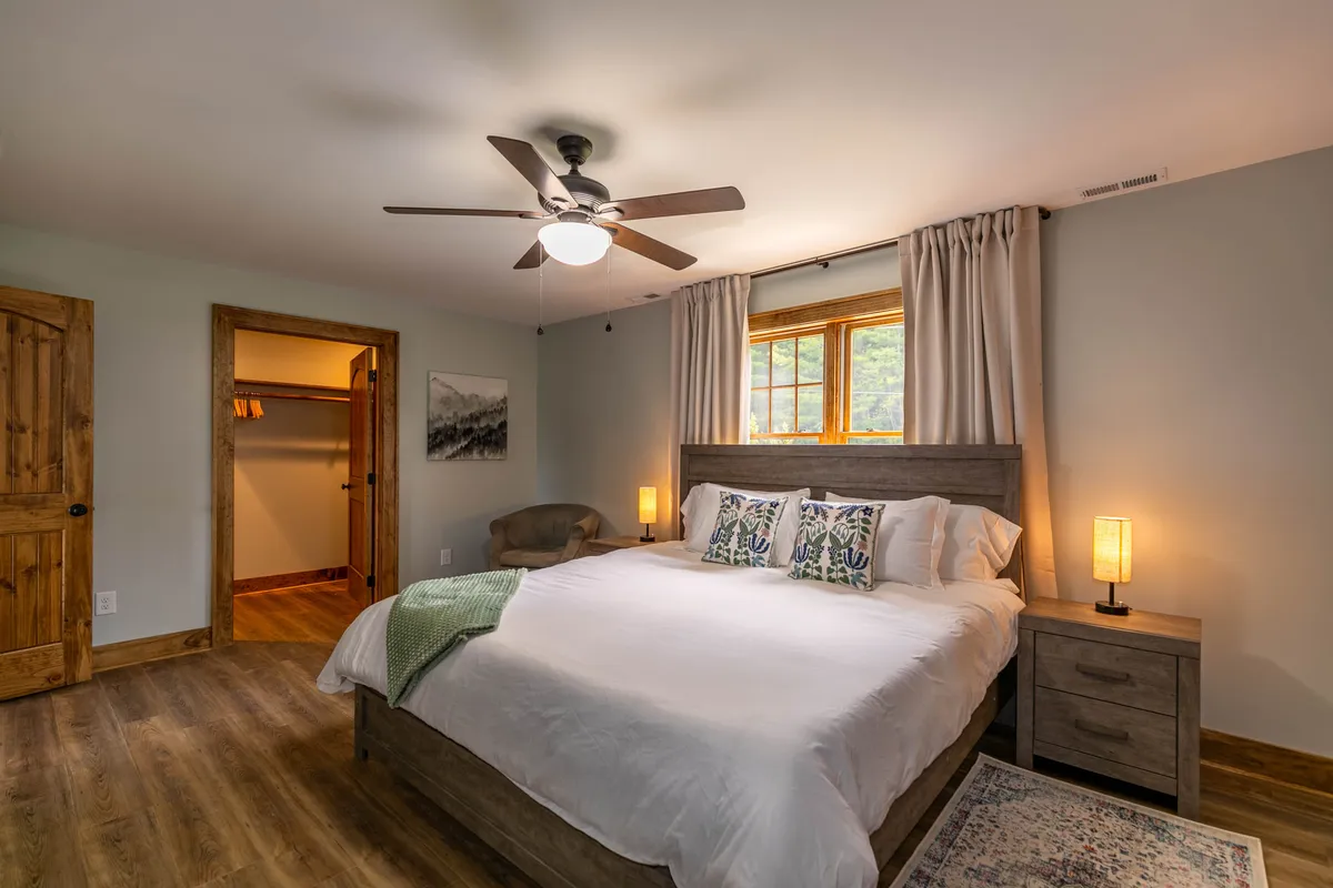 A beautifully appointed king-sized bed with plush pillows and nightstands, bathed in natural light from a curtained window. The room radiates tranquility and offers a restful, private retreat ideal for couples. Decorative accents and thoughtful lighting create a sense of luxury and calm.