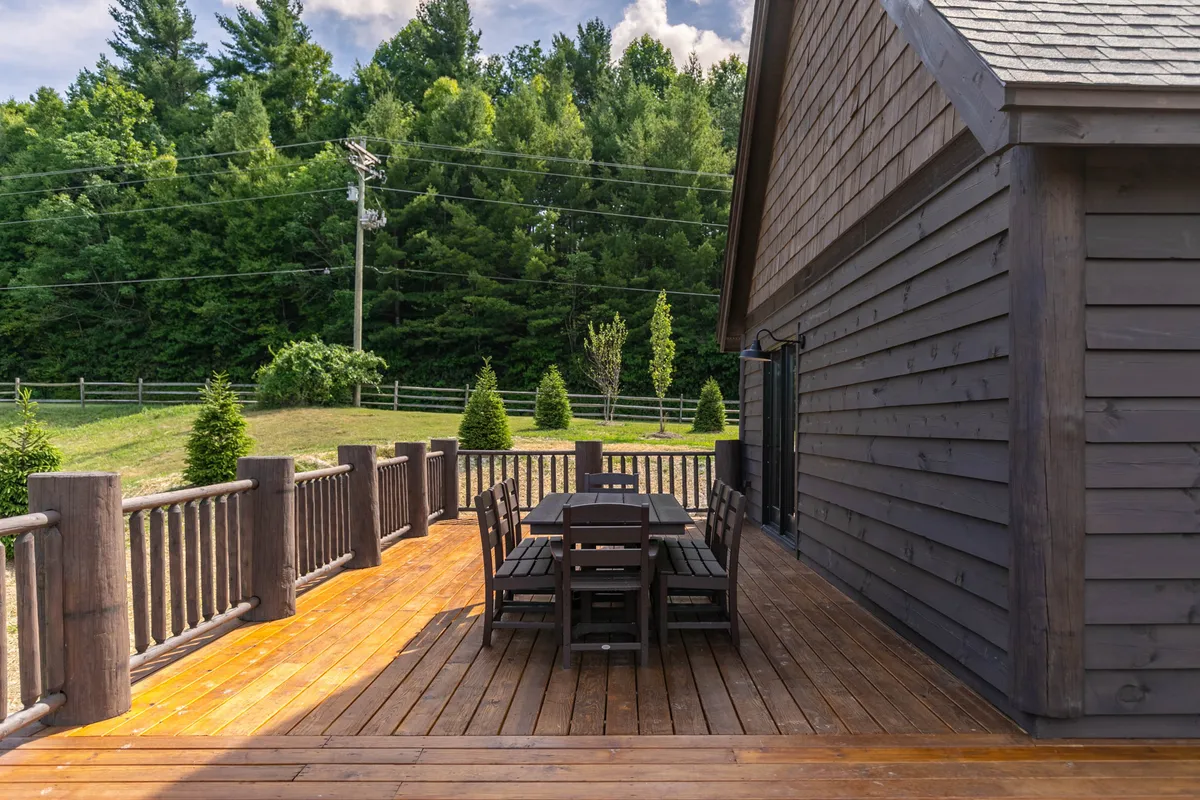 A spacious wooden deck set amidst lush trees, featuring a large dining table perfect for outdoor meals and gatherings. The area is bordered by a sturdy fence and offers a tranquil, nature-immersed setting ideal for evening festivities or relaxed family moments.