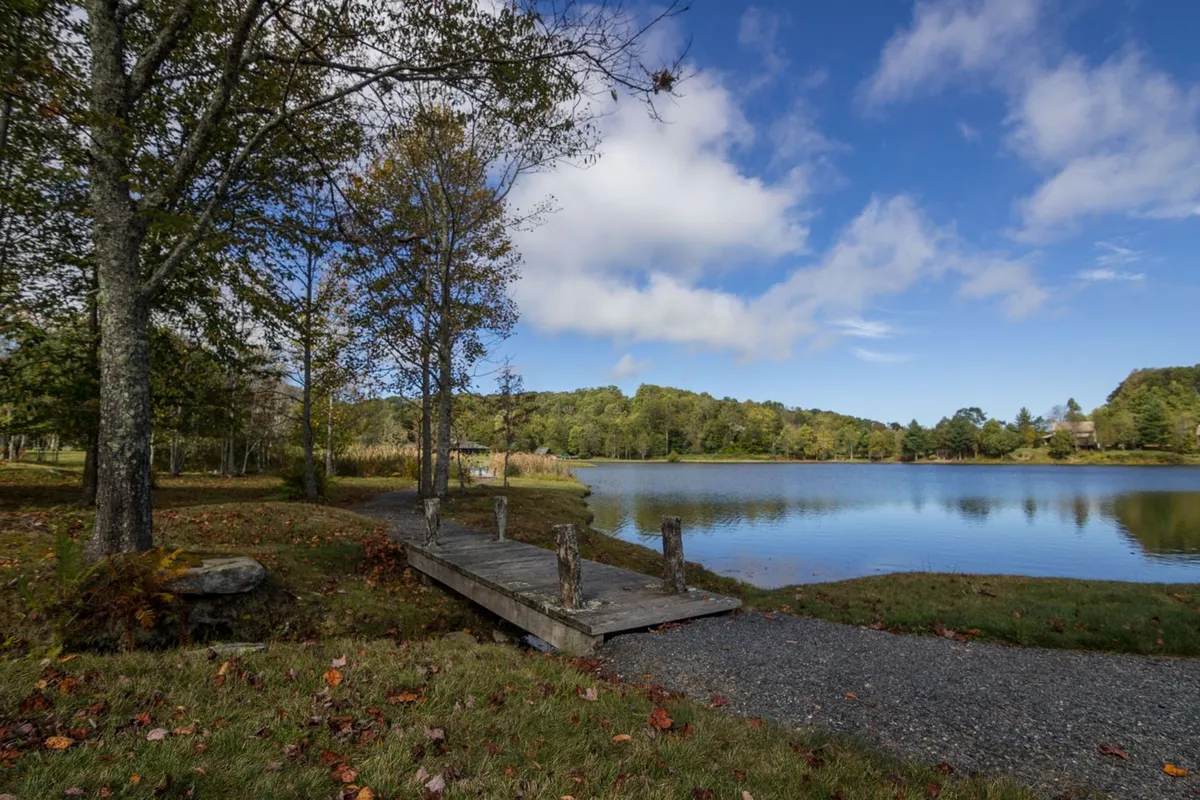 A peaceful scene featuring a wooden dock extending over a calm lake, surrounded by lush trees. The water reflects the sky, making it an inviting spot for outdoor activities or relaxation, with nature all around.