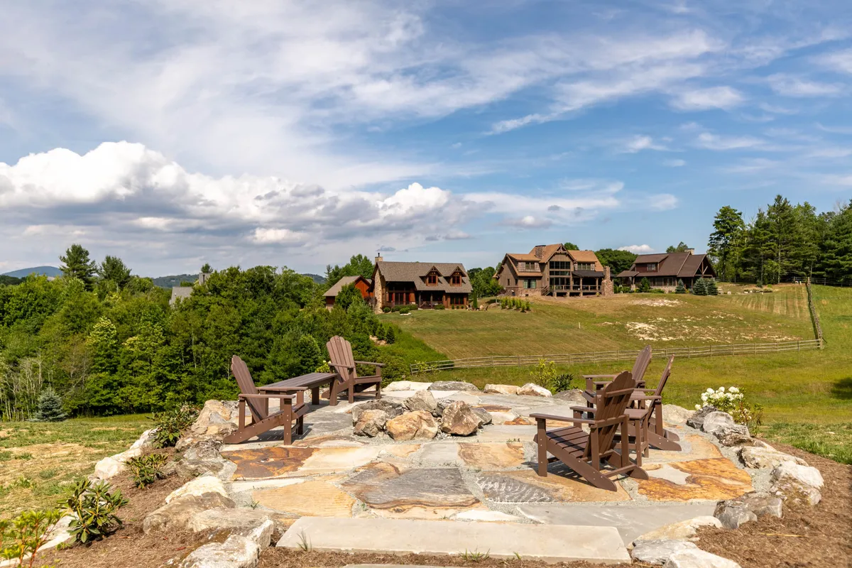 A peaceful stone patio set with wooden chairs overlooks a green landscape with distant houses and open sky. The scene radiates tranquility and invites activities like lounging, gathering with friends, and soaking in nature, suggesting a pet-friendly environment for walks and outdoor enjoyment.