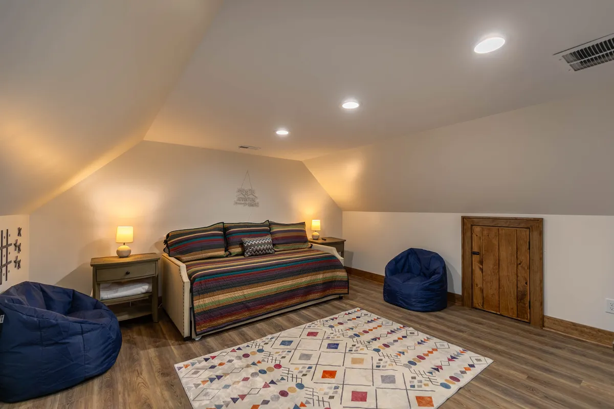 A cozy upstairs room furnished with a daybed, colorful striped bedding, bean bag chairs, and a decorative rug. The atmosphere is relaxed and adaptable, well-suited for extra guests, kids, or casual lounging.