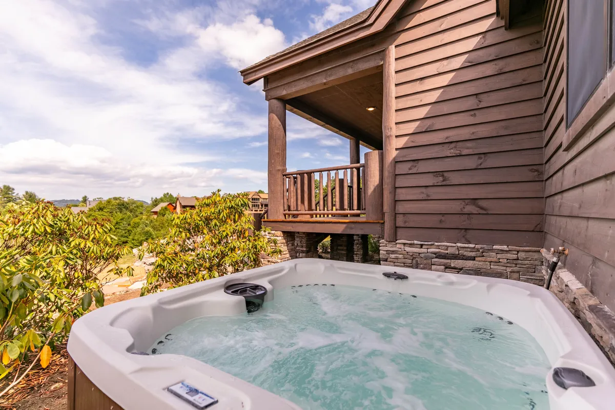 This image features a private hot tub situated on a wooden balcony overlooking a serene mountain landscape. The inviting waters of the tub are framed by the wooden railing and the natural beauty of the surrounding woodland, capturing a moment of true relaxation and seclusion.